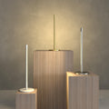 Three modern table lamps on wooden plinths against a neutral background